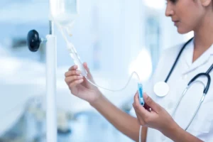 une infirmière en blouse blanche avec un stéthoscope autour du cou en train de régler une perfusion