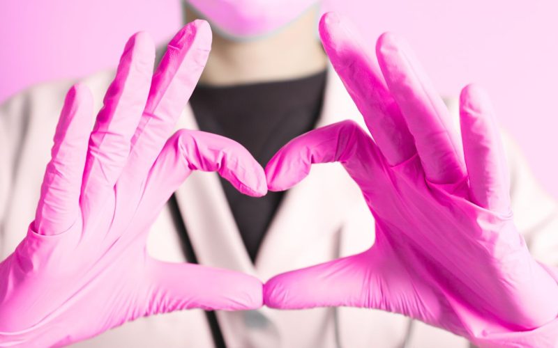 Les mains d'une infirmière dans des gants roses formant un coeur